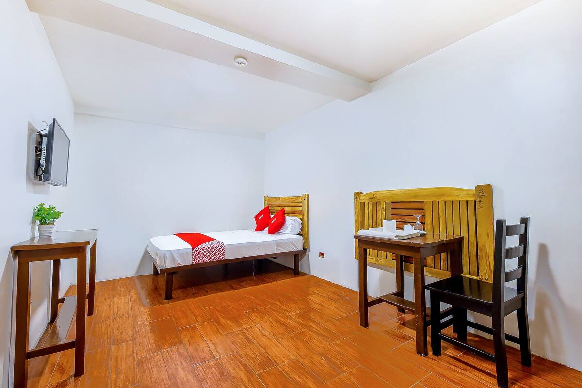 A small, clean room with a bed, a wooden table, and a chair.