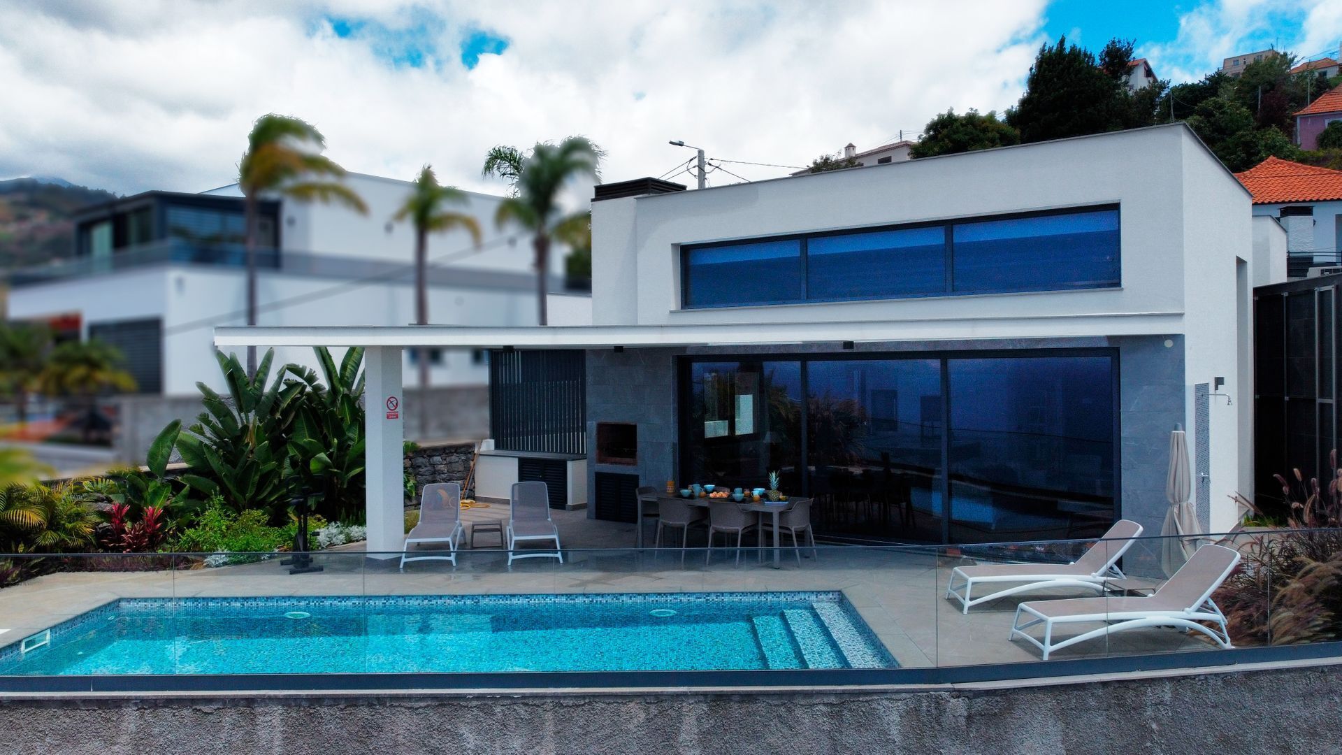 Una casa moderna de dos pisos con piscina, mobiliario exterior y ventanas amplias.
