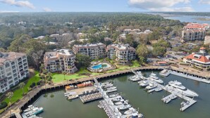 A marina with multiple boats docked, surrounded by residential buildings with balconies and a swimming pool. - Great Marina Views, Steps to Pool, Bike to Beach (Hilton Head Island)