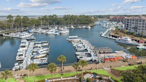 A marina with numerous boats docked, a pedestrian walkway, and a building with a red roof in the background. - Great Marina Views, Steps to Pool, Bike to Beach (Hilton Head Island)