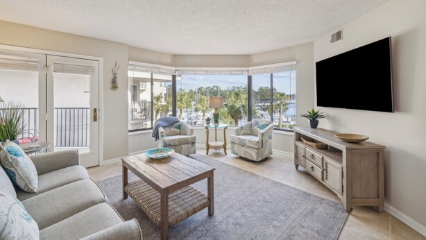 A spacious living room with a large window, a flat-screen TV, and a comfortable seating area. - Great Marina Views, Steps to Pool, Bike to Beach (Hilton Head Island)