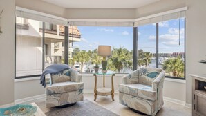 A corner room with two upholstered chairs, a small round table, and a view of a marina with boats and palm trees. - Great Marina Views, Steps to Pool, Bike to Beach (Hilton Head Island)