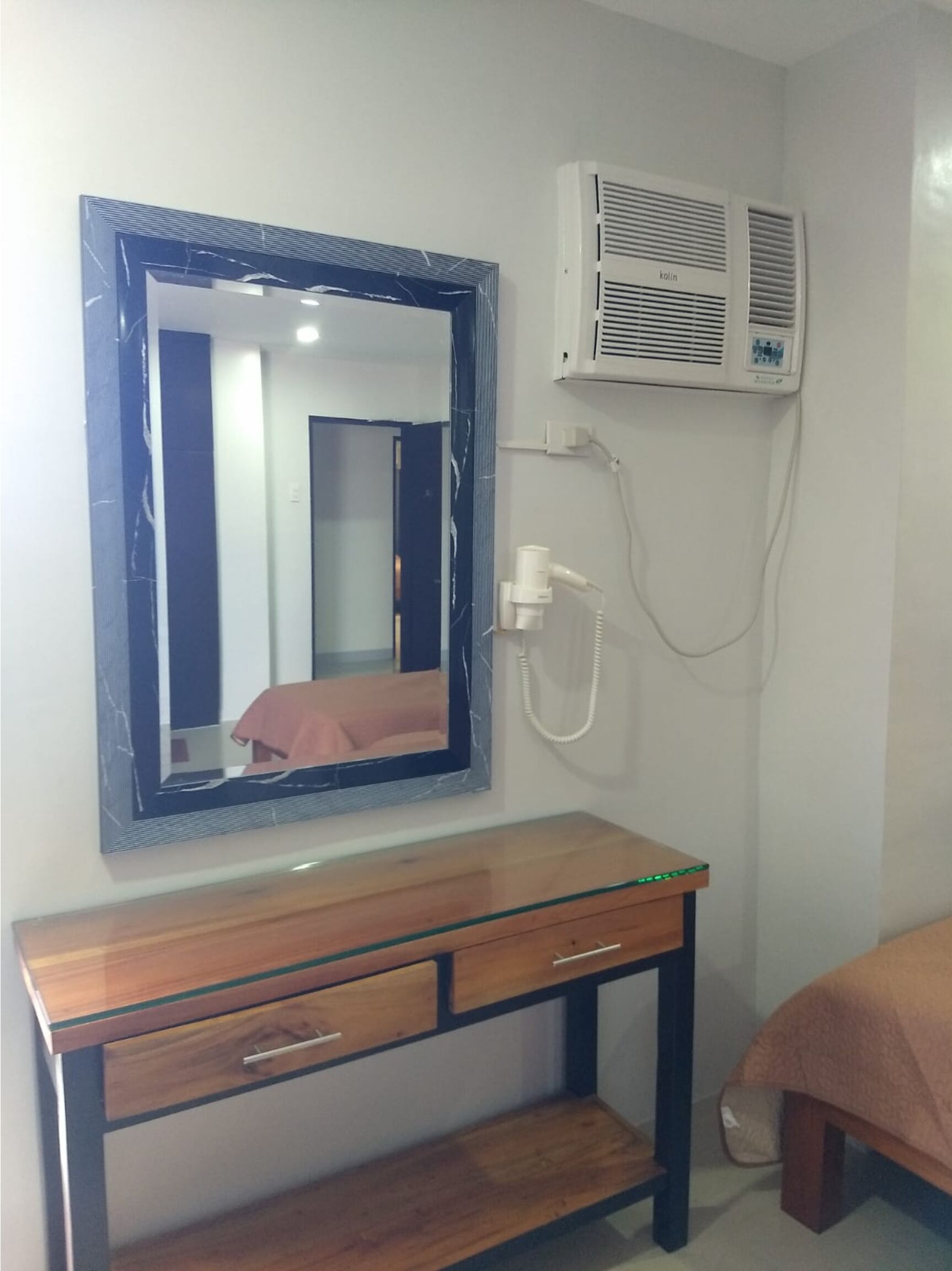 Un dormitorio con una mesita de noche de madera, un espejo, aire acondicionado de pared y una cama con manta.