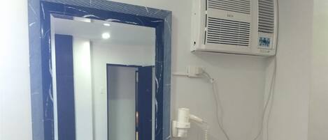 Un dormitorio con una mesita de noche de madera, un espejo, aire acondicionado de pared y una cama con manta.