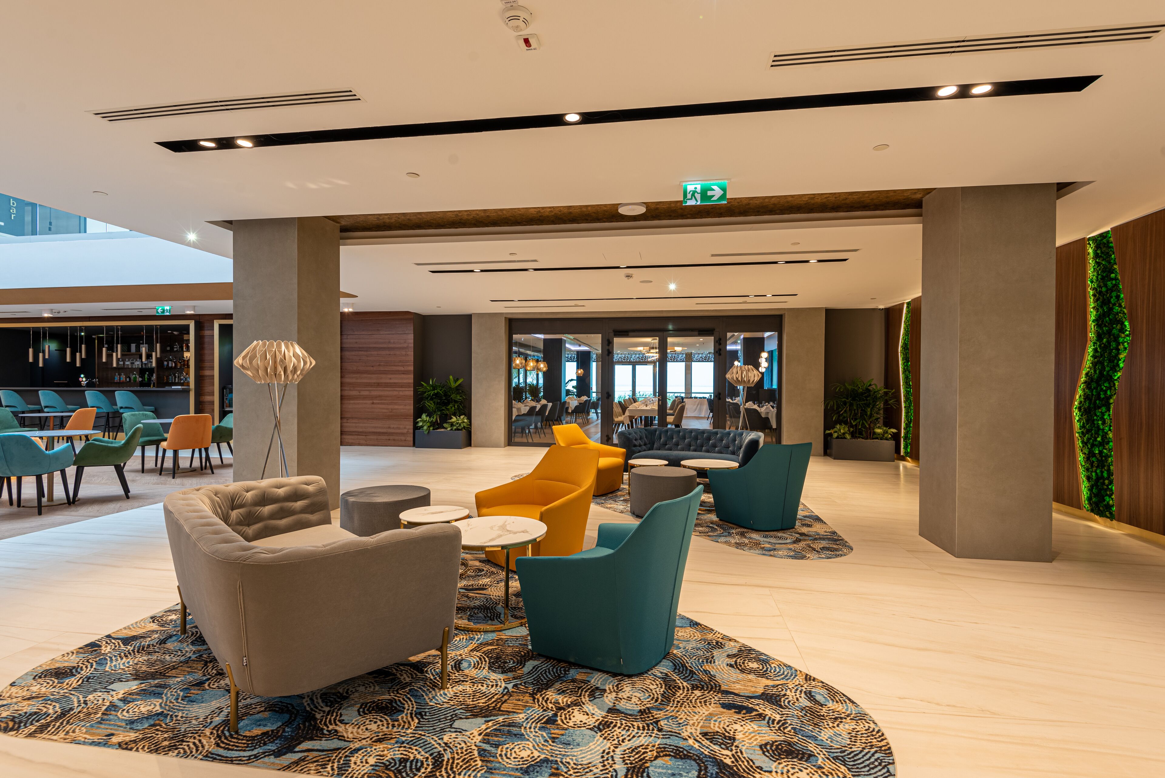 A modern lobby with seating areas, a bar, and a green wall.
