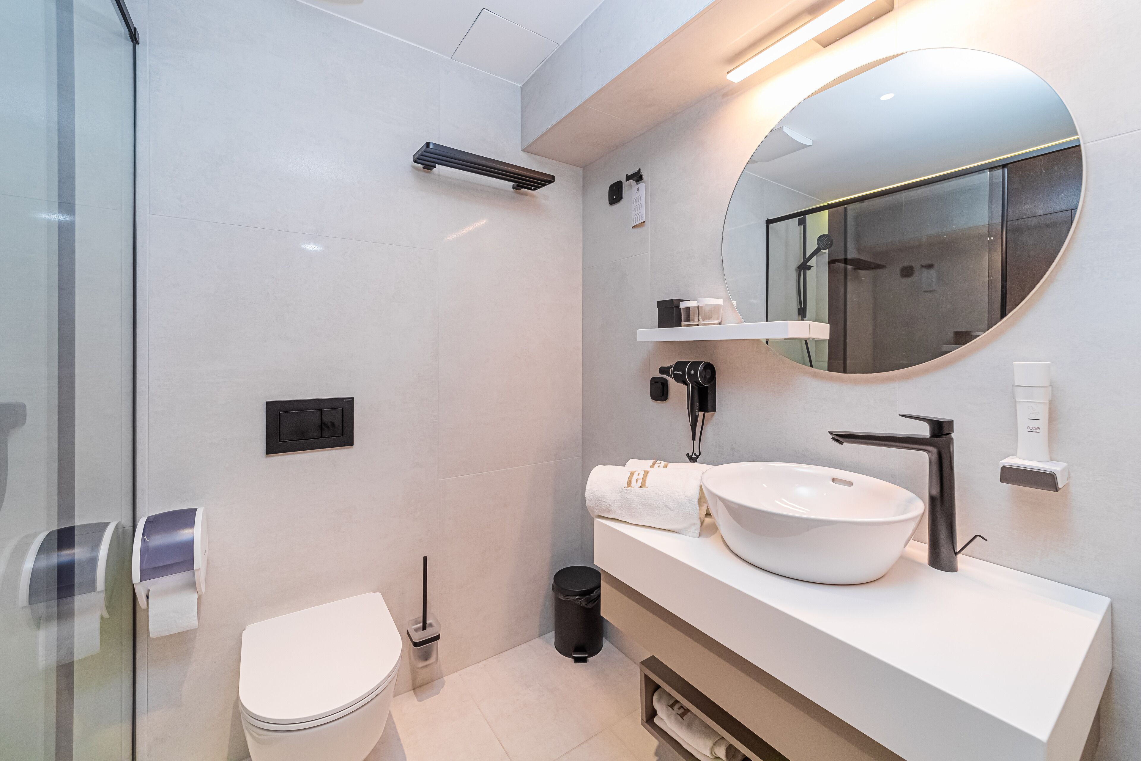 A modern bathroom with a glass shower enclosure, a white sink with a large mirror, and a toilet.
