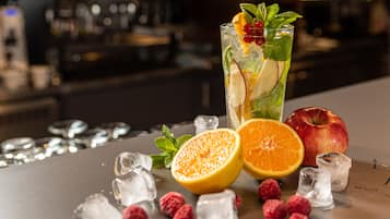 Eine Bar mit einem hohen Glas, das einen Cocktail enthält, garniert mit Früchten und Minze, umgeben von Eiswürfeln, einer halben Orange, einem ganzen Apfel und Himbeeren.