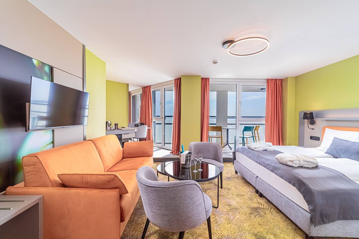 Ein Hotelzimmer mit Sofa, Bett, Tisch mit Glasplatte und Fernseher.