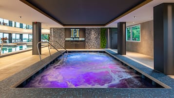 A modern indoor pool with a colorful water feature, surrounded by a contemporary design with large windows and a view of the outdoors.