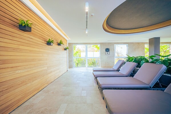 A spa room with wooden paneling, a ceiling light, a clock, and sun loungers.