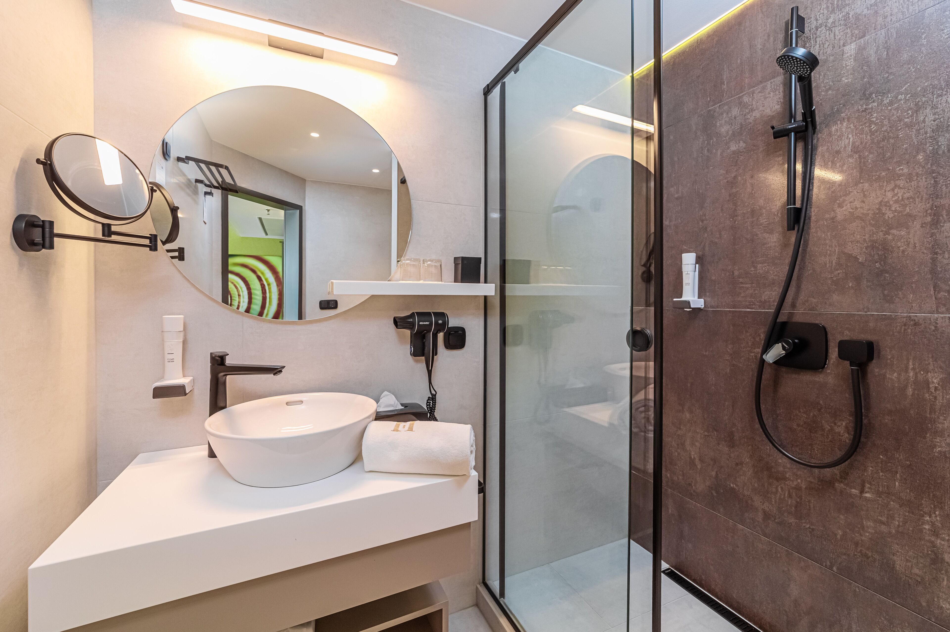 A modern bathroom with a white sink, a round mirror, a handheld showerhead, and a glass-enclosed shower.