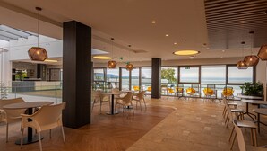Un comedor moderno con mesas y sillas, ventanas amplias y vista al mar.