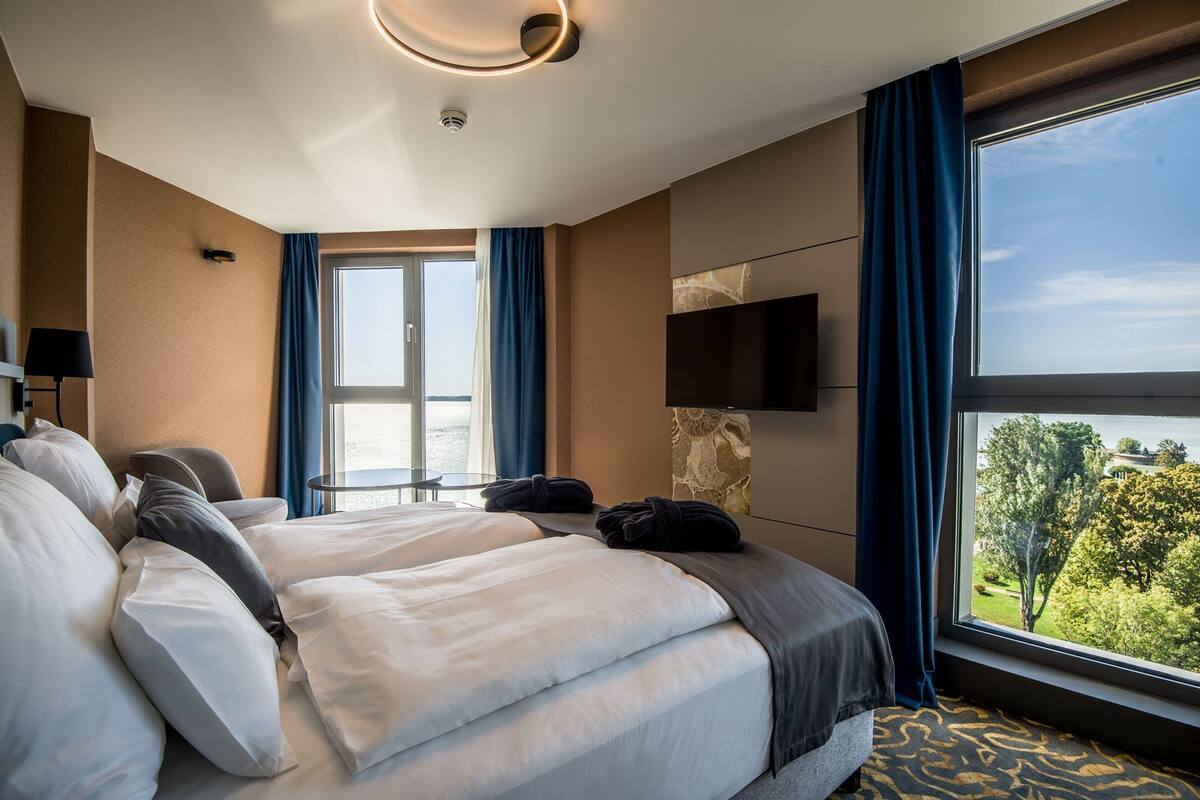 Ein Hotelzimmer mit einem großen Bett, einem Flachbildfernseher, einem Schreibtisch und Blick auf ein Gewässer und Grünflächen.