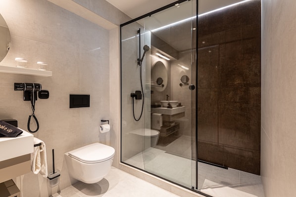 A modern bathroom with a glass-enclosed shower, a toilet, and a sink with a towel rack.