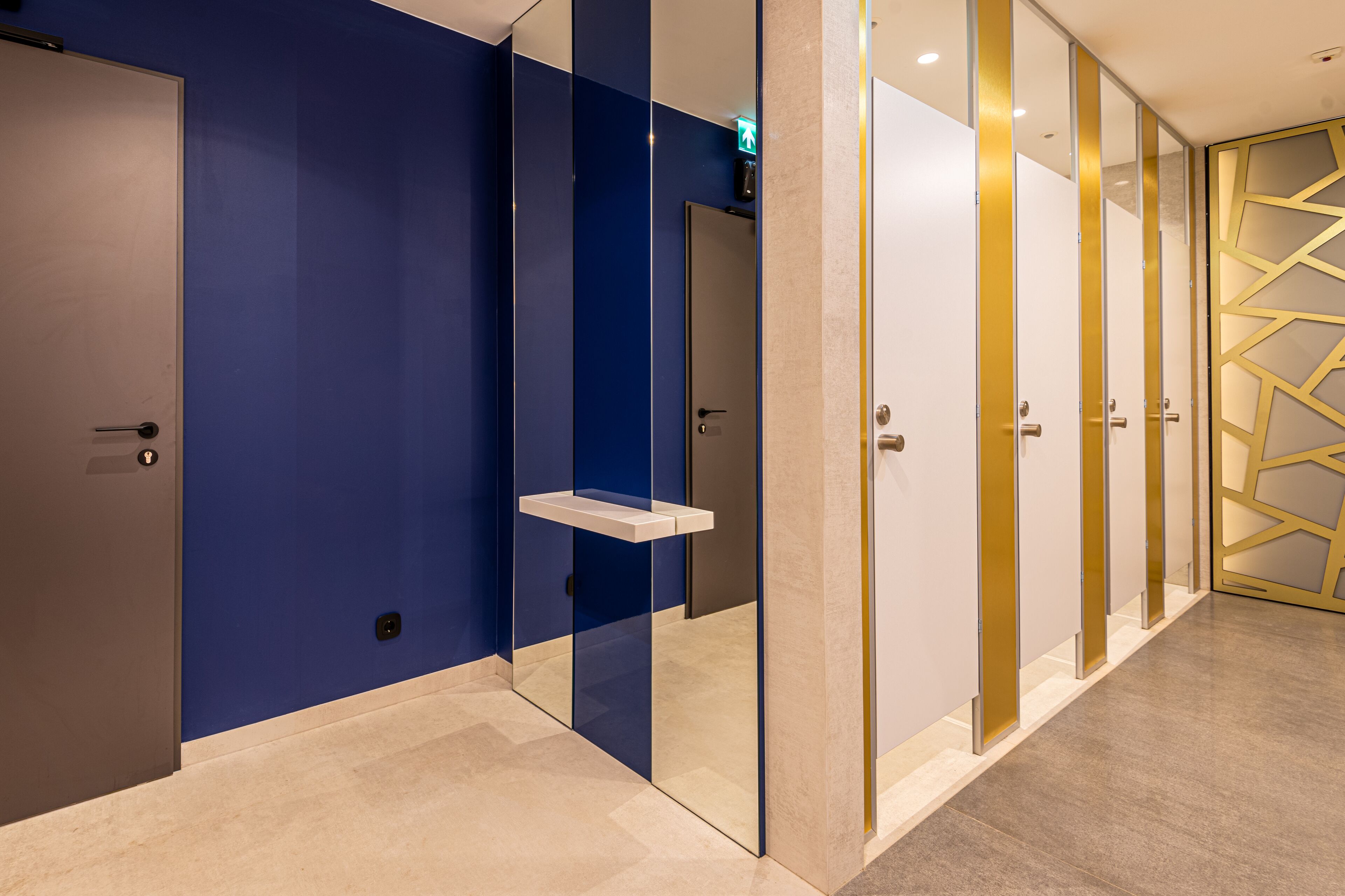 Un couloir d’hôtel moderne aux murs bleus et blancs, avec une cloison en verre et un mur orné d’un motif géométrique sur le côté droit.