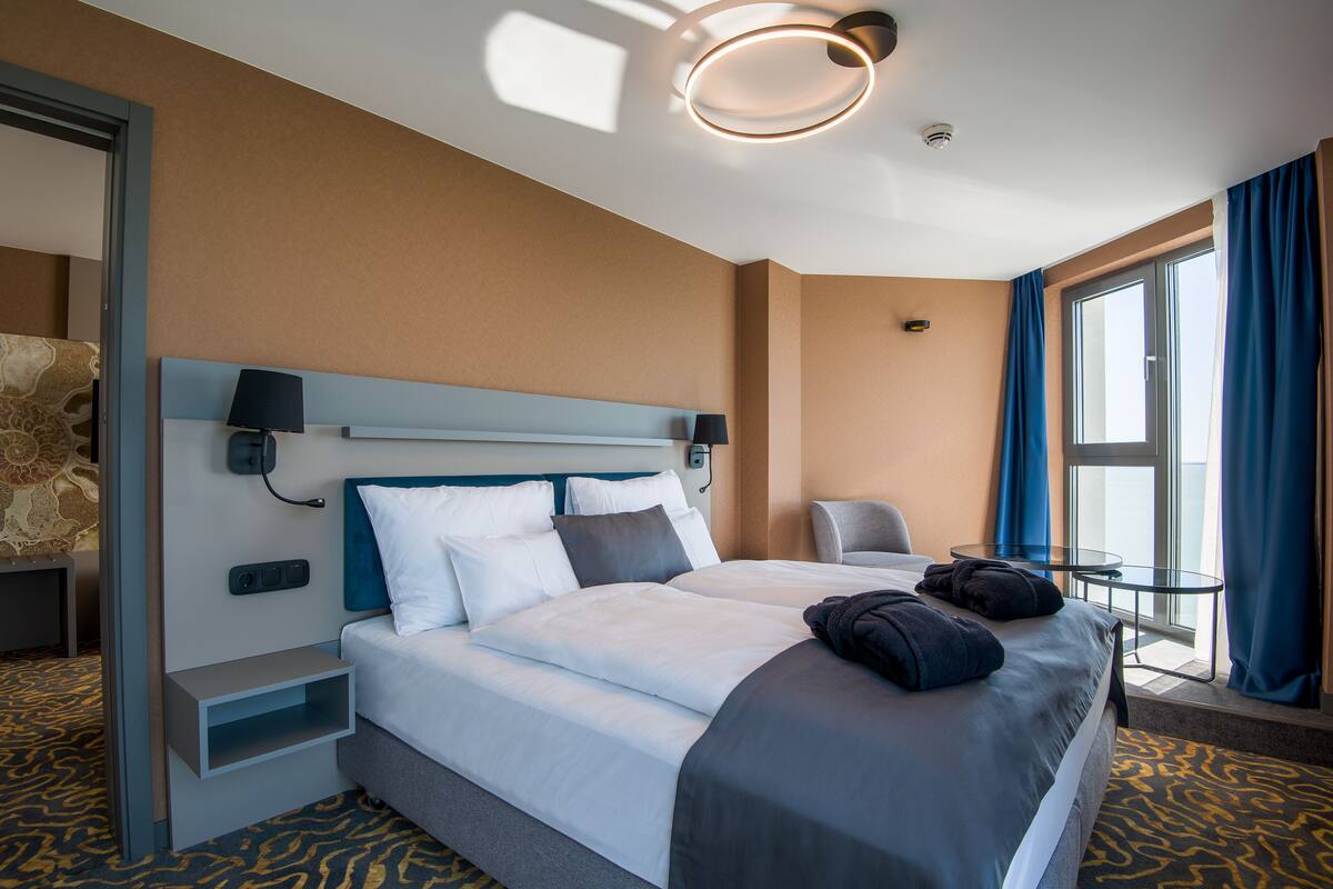 Ein Hotelzimmer mit einem großen Bett, einem Nachttisch, einer Lampe, einem Sessel und einem kleinen Tisch.