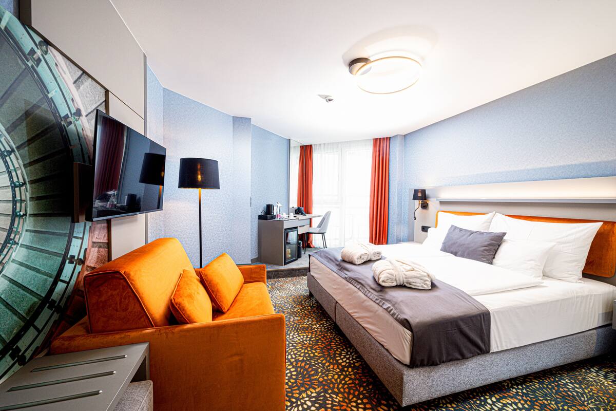 Ein Hotelzimmer mit einem Bett, einem orangen Sofa, einem Schreibtisch und einem Fernseher.