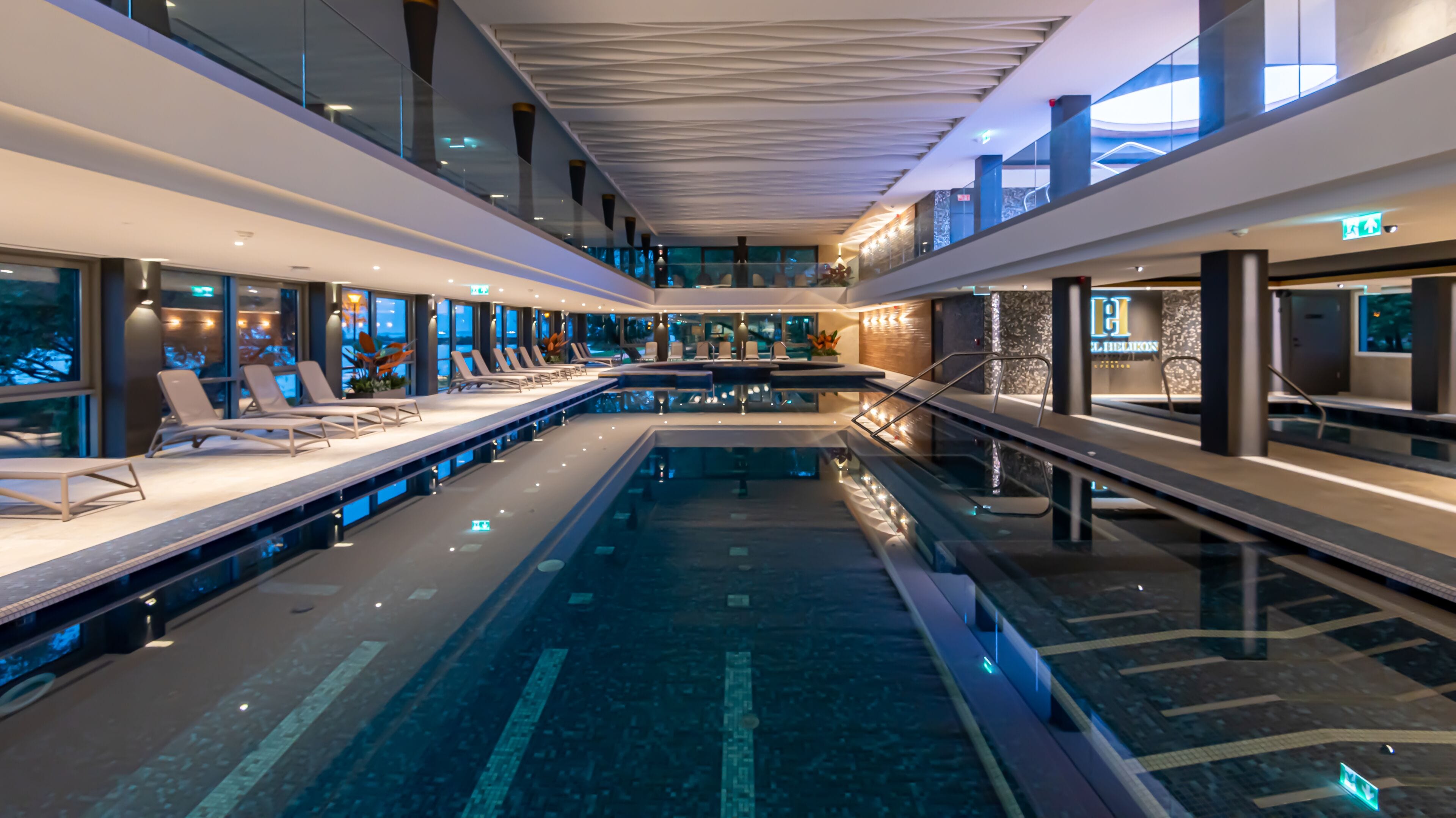 A modern indoor swimming pool with lounge areas on either side, large windows, and a contemporary design.