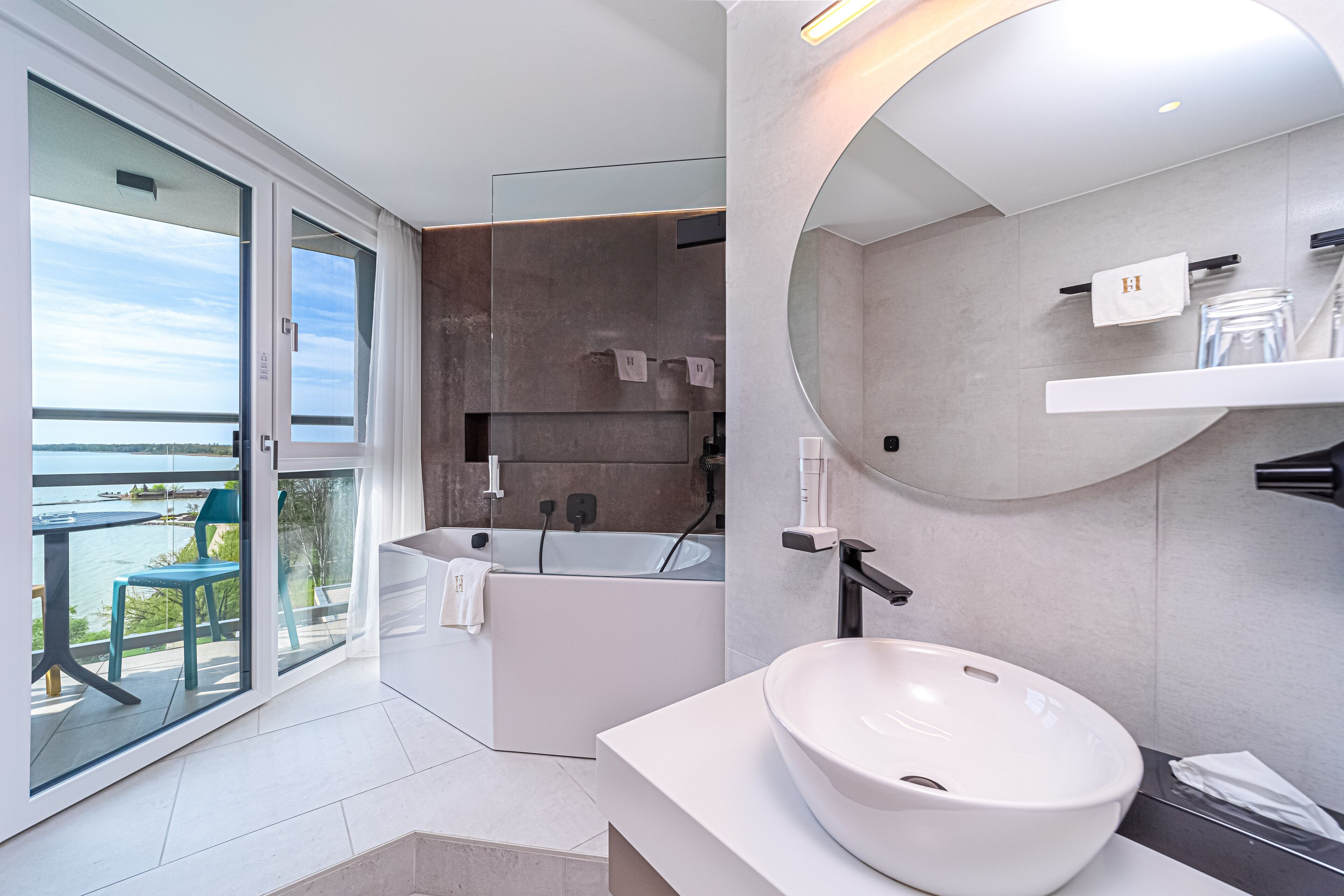 Un baño moderno con una bañera grande, un espejo redondo y un lavabo blanco.