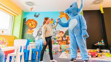 Niño interactuando con un personaje promocional en una sala con murales coloridos, pequeñas mesas y sillas.