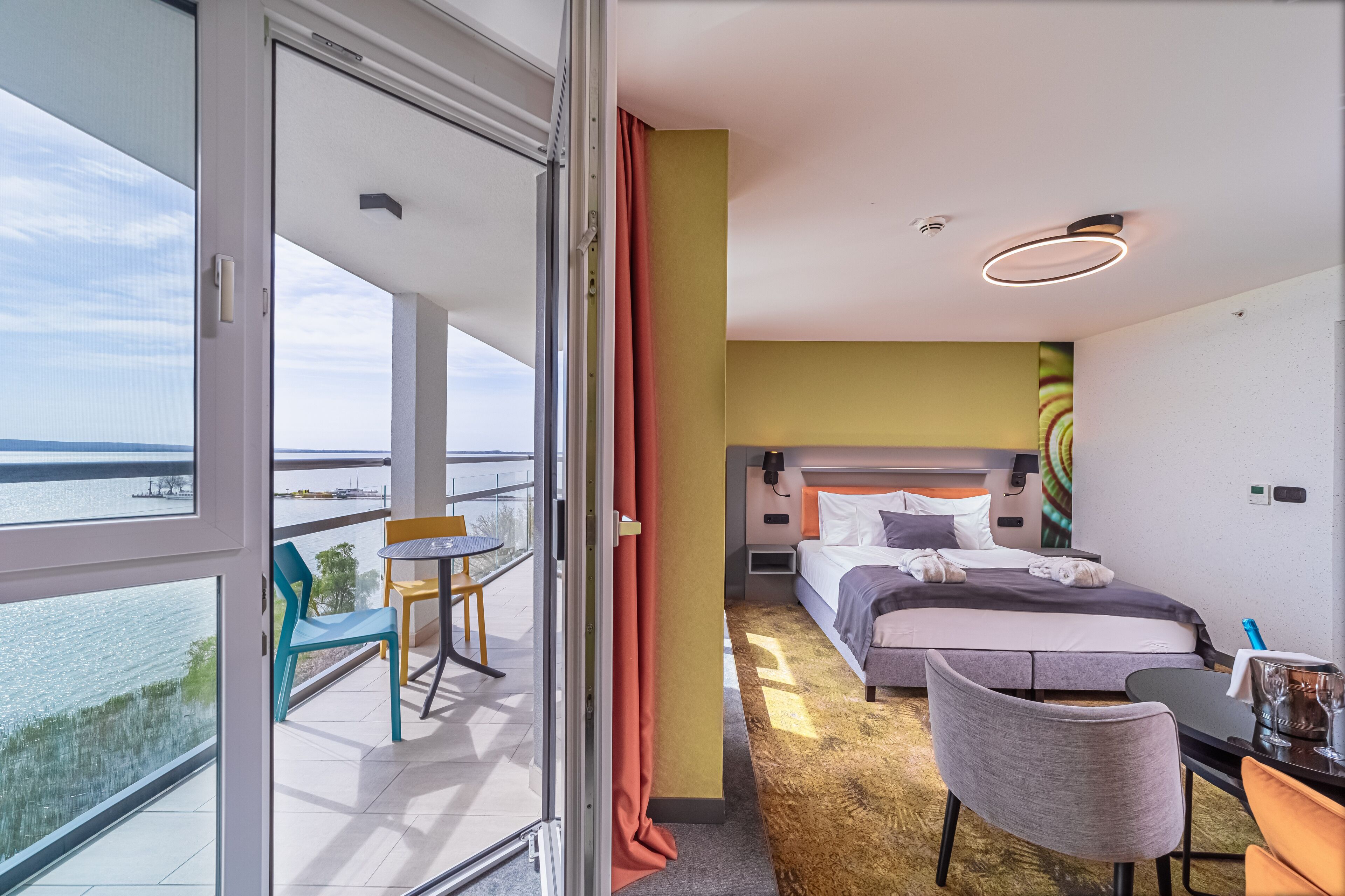 A hotel room with a balcony, a bed, a desk, and a chair.