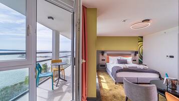 A hotel room with a balcony, a bed, a desk, and a chair.
