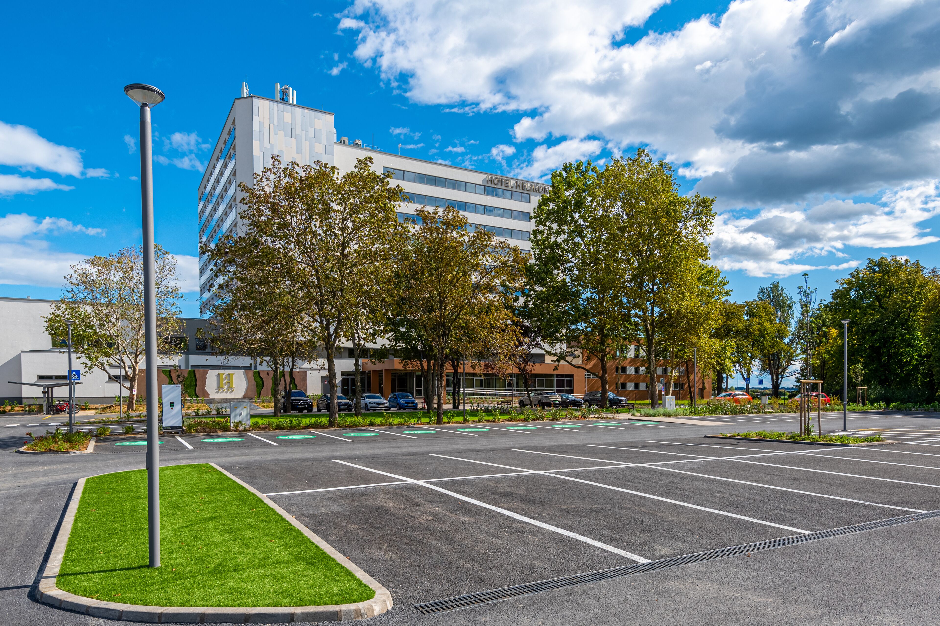 A hotel with a modern design, a parking lot, and surrounding greenery.