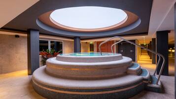 Un jacuzzi de varios niveles con un tragaluz circular encima, rodeado de un suelo de baldosas y una escalera que sube.