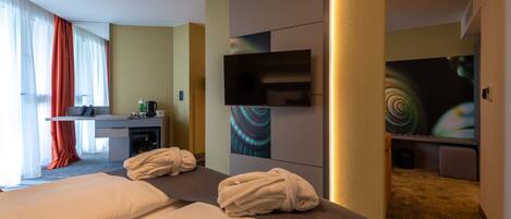 A hotel room with two beds, a desk, a TV, and a bathroom.