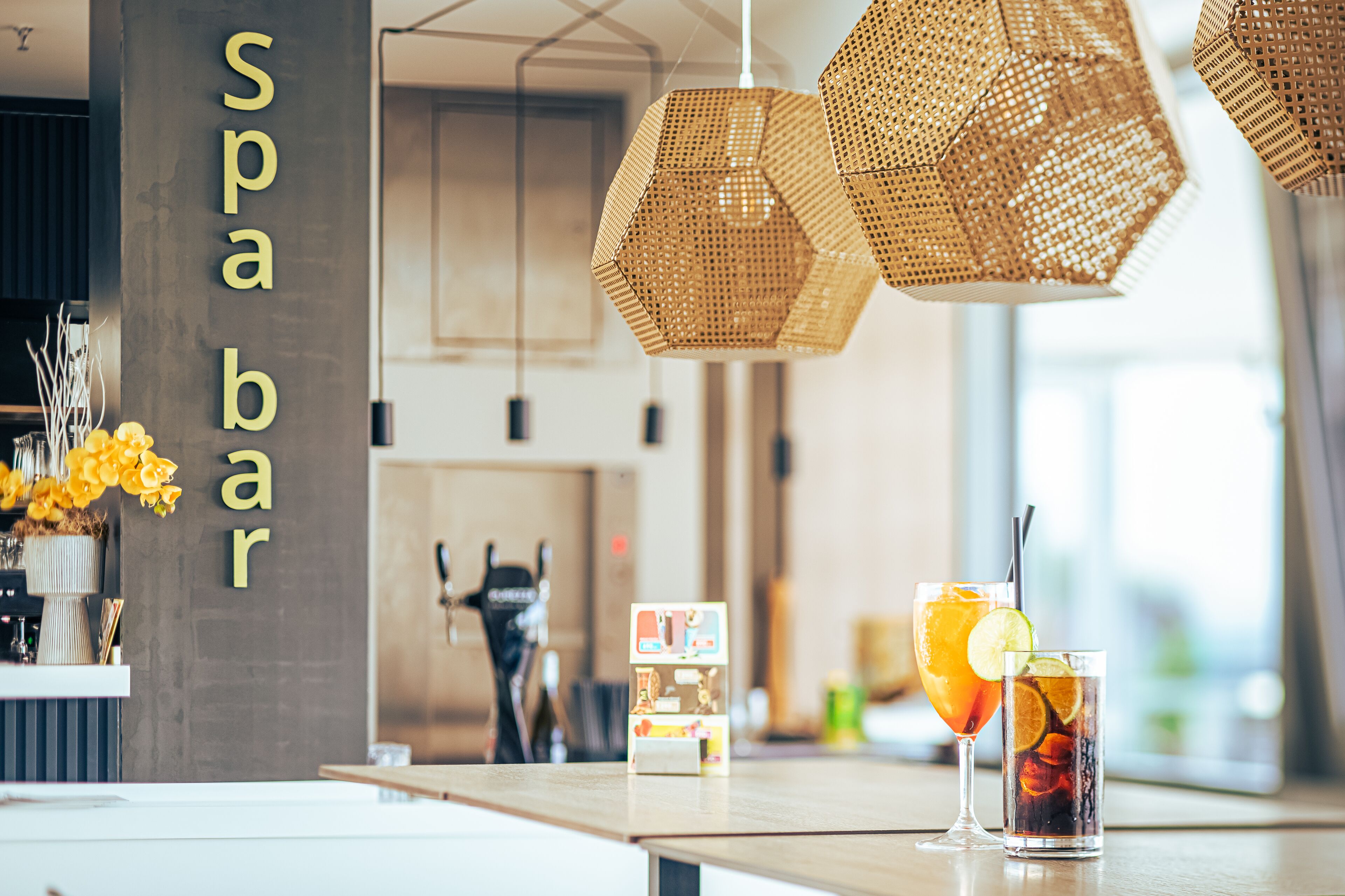 Zona de bar con lámparas colgantes de mimbre, un minibar y dos bebidas sobre la barra.