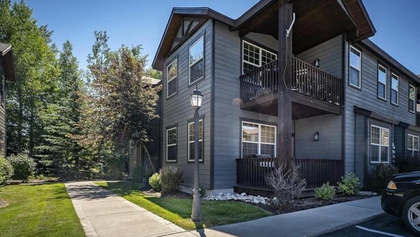 A two-story building with a balcony on the second floor, a visible garage door, and a well-maintained lawn. - Perfect Mountain Family Condo Near Grand Targhee and Driggs (Driggs)