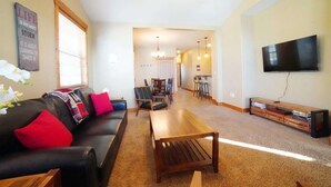 A living room with a sofa, coffee table, TV, and a dining area with chairs and a table. - Perfect Mountain Family Condo Near Grand Targhee and Driggs (Driggs)