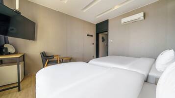 Een hotelkamer met twee bedden, een bureau met stoel, een televisie en een airconditioning.
