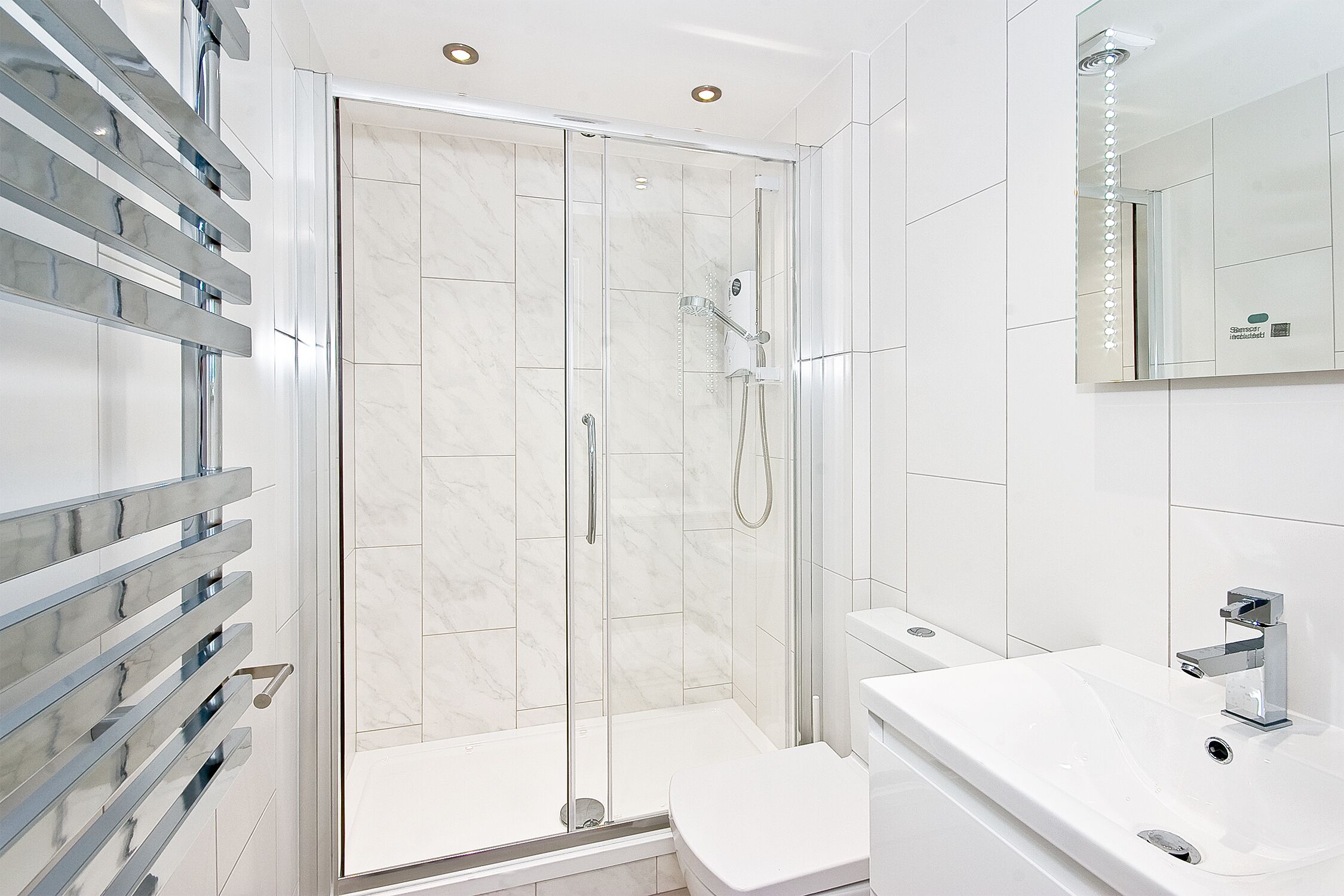 Een moderne badkamer met een douchecabine van glas, een witte wastafel en een grote spiegel.