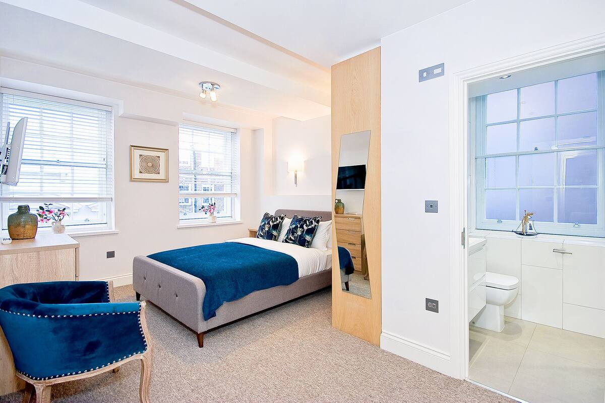Une chambre à coucher comprenant un lit, une chaise, une commode et une salle de bain avec des toilettes et un lavabo.