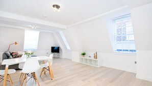 A modern living room with a dining area, large windows, and a flat-screen TV.