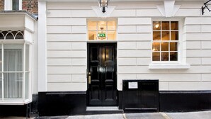 A white building with a black door, a sign above the door, and a window to the right.