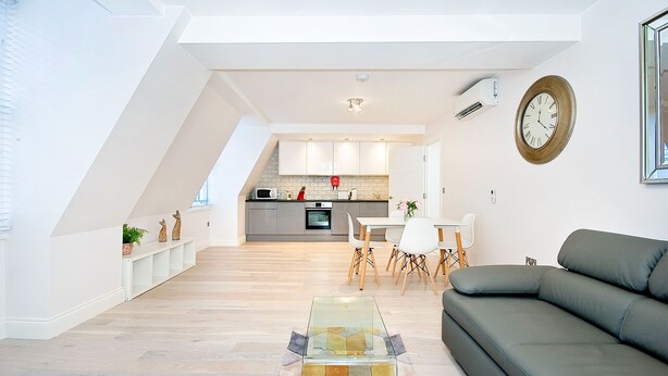 A modern living room with a glass coffee table, a grey sofa, and a dining area with a white table and chairs.