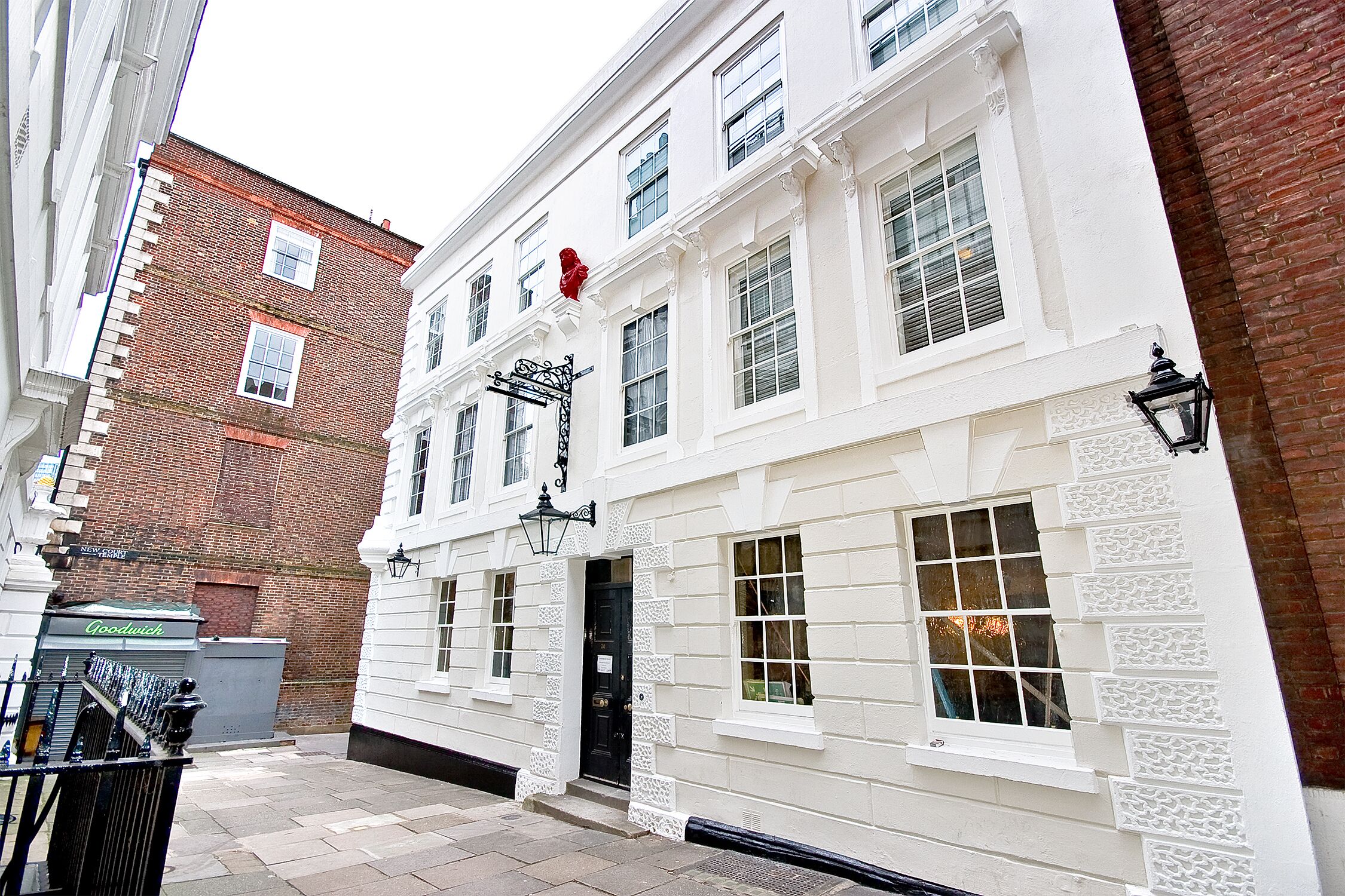 A white building with a black door and windows, a brick wall, and a street lamp.