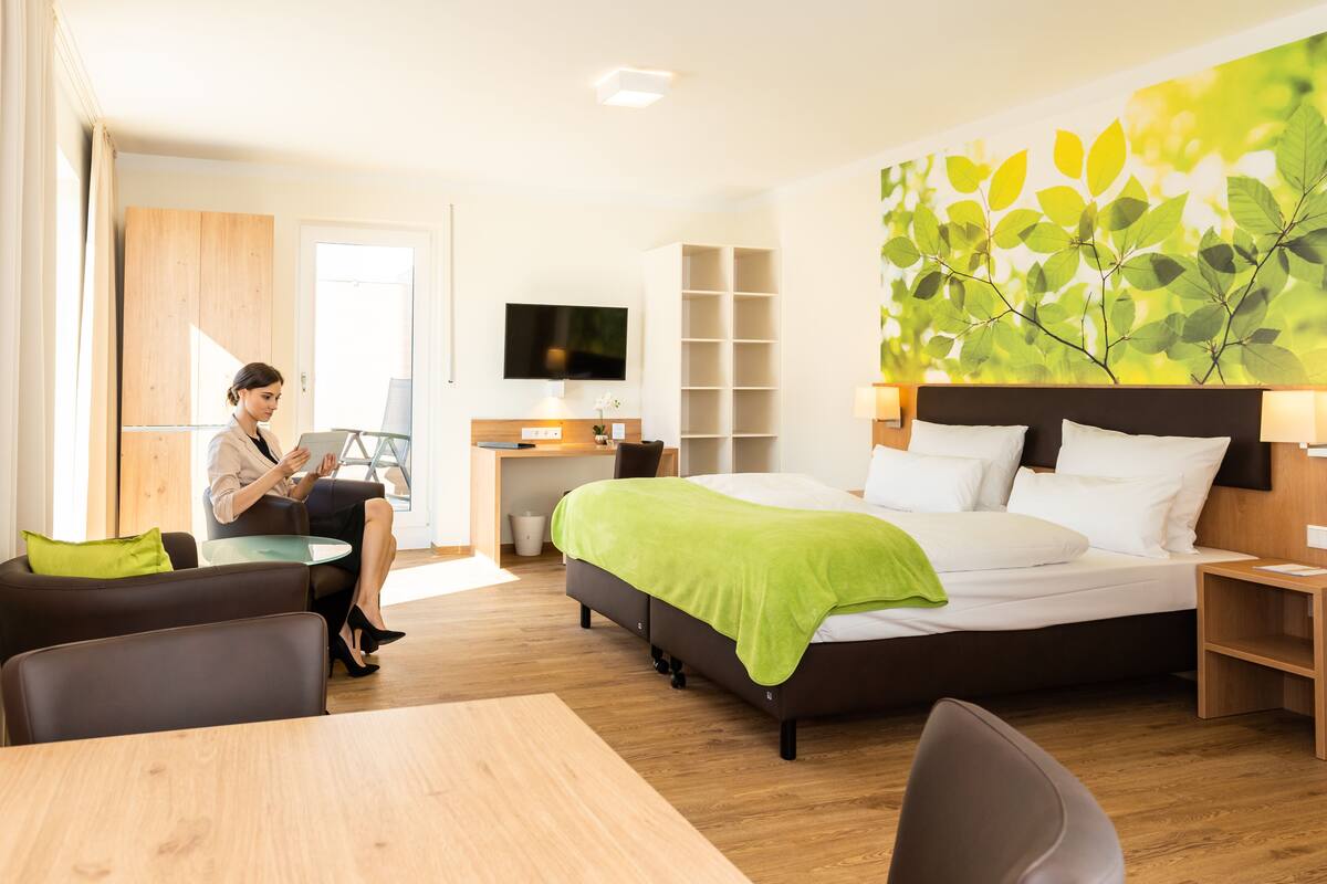 A modern hotel room with a bed, a desk, a television, and a large window.