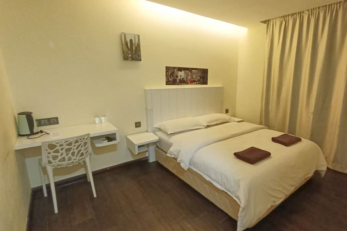 A hotel room with a bed, a desk, and a chair. There is a painting on the wall and a curtain on the window.