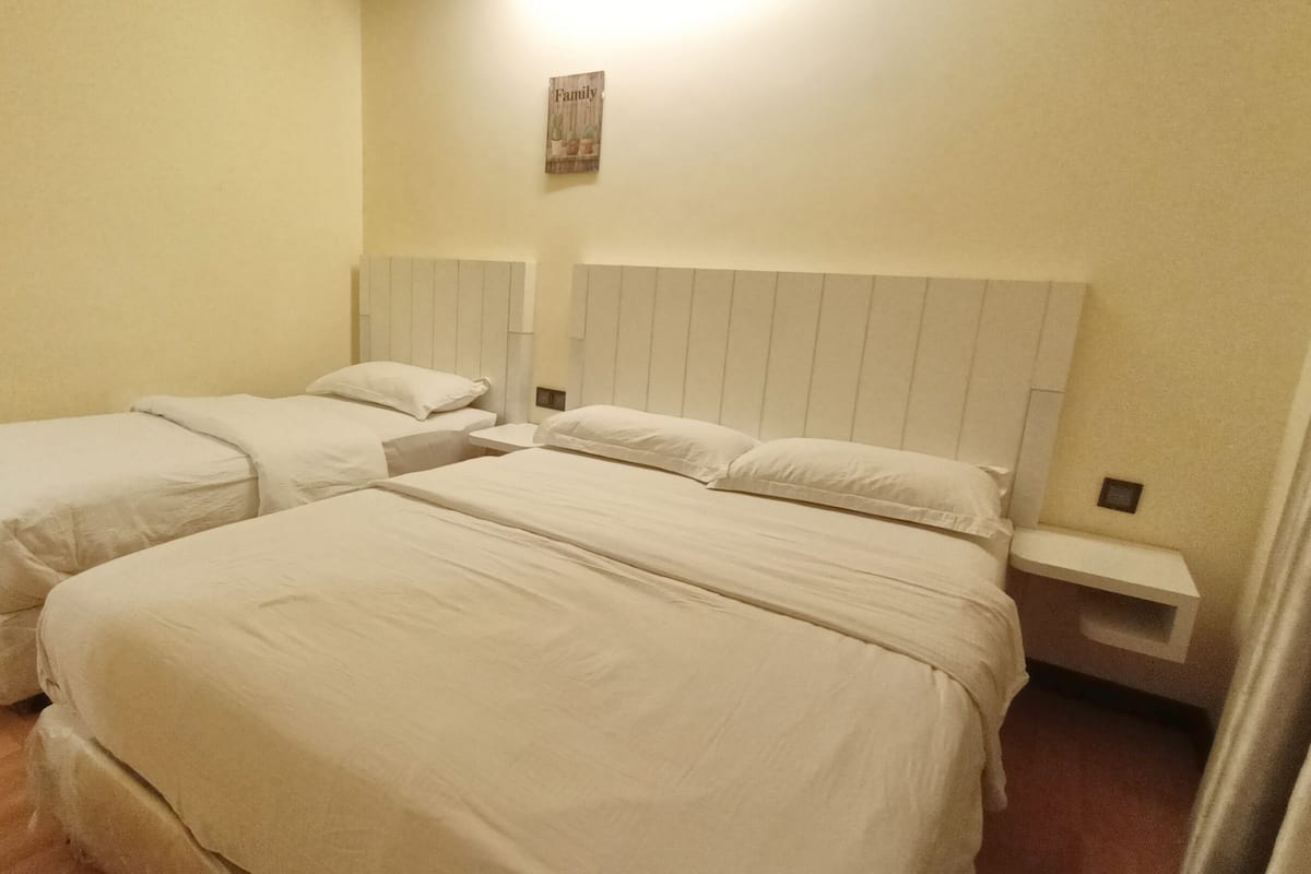 A hotel room with two single beds and a larger bed, all with white linens.