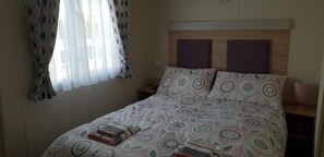 Une chambre à coucher avec un lit, une table de chevet, une lampe et une fenêtre avec des rideaux.
