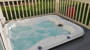 Een hottub met een houten terras en een witte omheining.