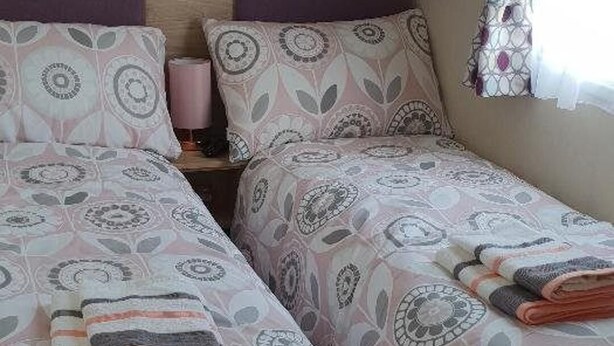 Een kamer met twee bedden, elk voorzien van beddengoed met een patroon, een houten hoofdbord en een raam met gordijn.