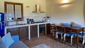 A compact kitchen with a stove, oven, and microwave. There is a dining table with chairs and a blue-striped cushion. - Beautiful villa in the park of Elba Island (Redinoce)