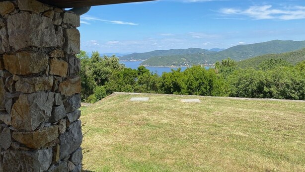 A stone wall with a view of a grassy area and a body of water in the distance. - Beautiful villa in the park of Elba Island (Redinoce)
