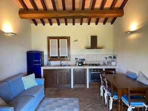 A compact kitchen with a dining area, wooden beams on the ceiling, and a blue refrigerator.