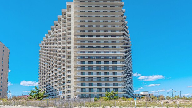 Un immeuble de grande hauteur doté d’une façade incurvée originale, de nombreux balcons et, en arrière-plan, un ciel d’un bleu éclatant.