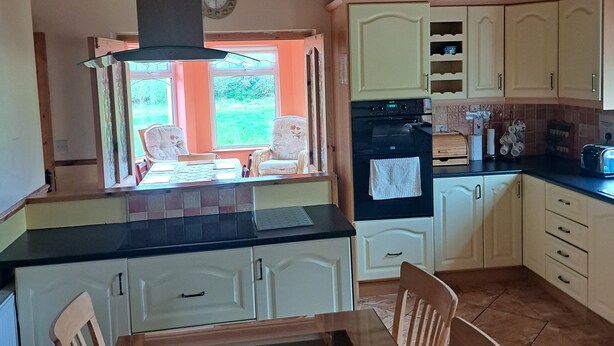 A kitchen with wooden cabinets, a black countertop, and a dining table with chairs. - Spacious 6-bed House 10 Minutes From Knock Airport (Kilmovee)